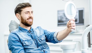 Man smiling at reflection in handheld mirror