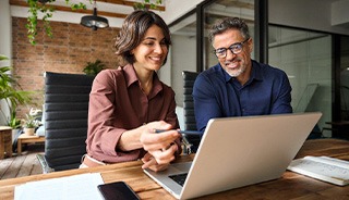 Man and woman smiling while reviewing information on laptop