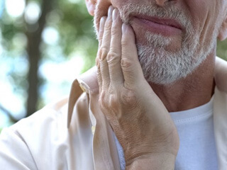 an older man holding his jaw due to tooth pain